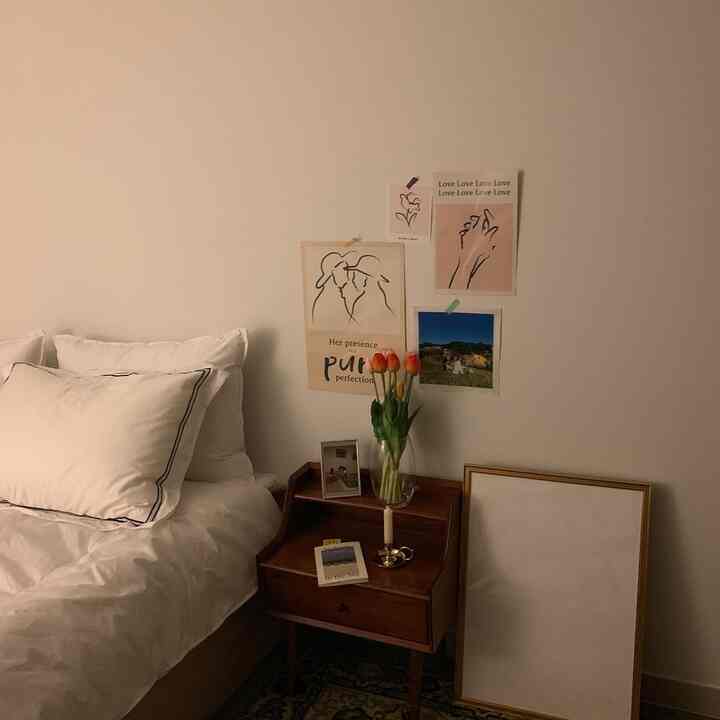 Cozy bedroom with warm wood tones and white colors, featuring a nightstand with a vase and posters decorating the wall