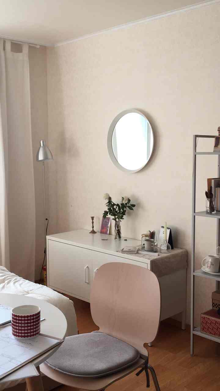 Cozy living room with warm wood tone flooring, white furniture, and round mirror on the wall