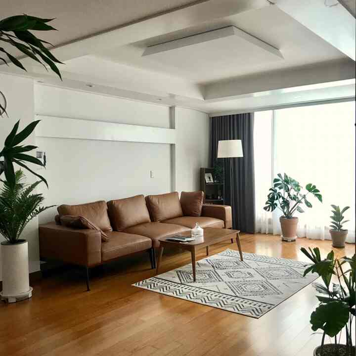 Warm wood tones living room featuring a brown leather sofa, multiple plants, curtains, and cafe-style decor