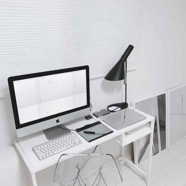 A white and transparent home office space featuring a computer desk and ghost chair in a clean simple modern interior