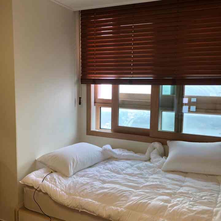 A bedroom with white and wood tones, featuring neatly arranged white bedding and wooden blinds creating a calm atmosphere