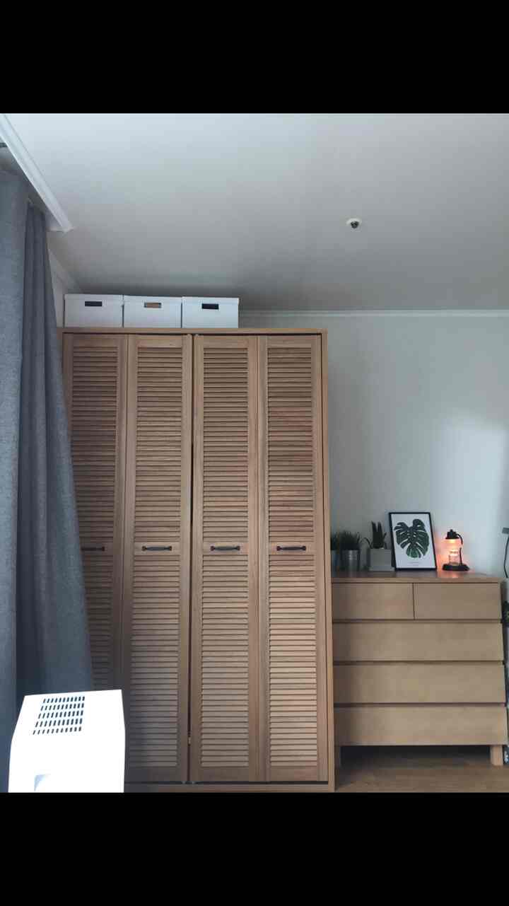 Natural colored bedroom space featuring a wooden wardrobe and dresser bathed in natural light creating a cozy atmosphere