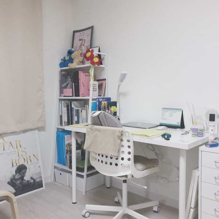 ホワイトトーンのコンパクトな部屋で、デスク、チェア、棚、額縁が配置されたモダンなホームオフィス