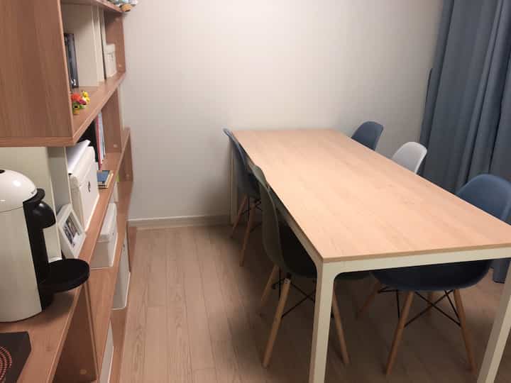 Modern dining room with natural wood tones and blue curtains, featuring a dining table and bookshelf in a multi-purpose space