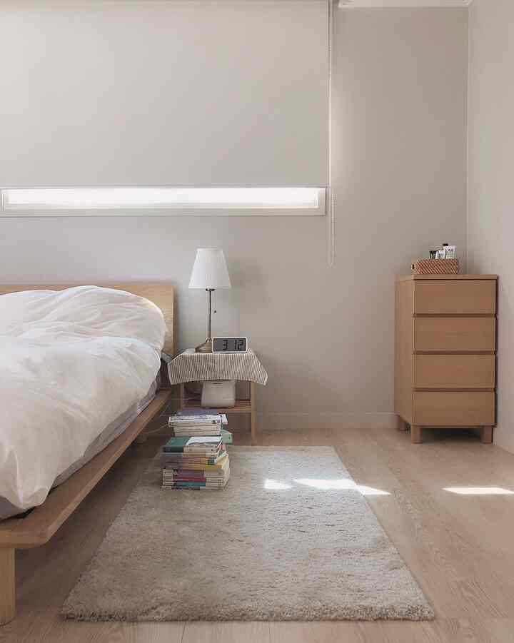 ベージュ色の壁と白い寝具の寝室、オーク材のベッドフレームとナイトテーブルが配置された清潔でモダンな空間