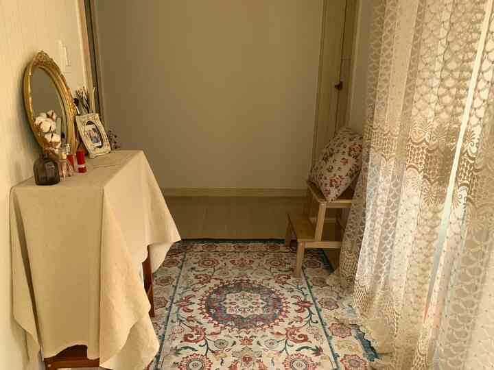 ベージュとアイボリーの色調の小さなウォークインクローゼット、ペルシャパターンのラグと木製ステップスツール、化粧台が配置されたナチュラルな雰囲気のインテリア