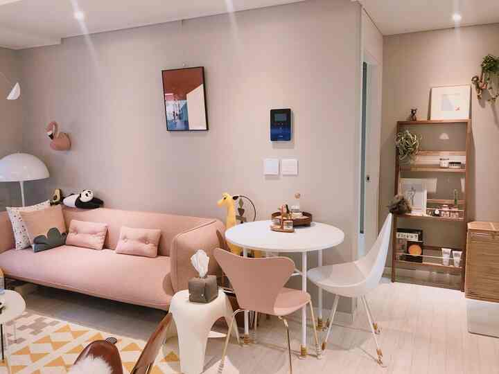 A cozy and bright living room in pink and natural tones featuring various decor items and a dining table