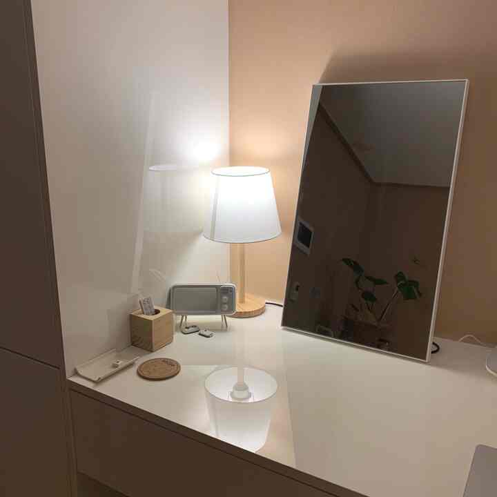 A simple, cozy vanity space in white and natural tones featuring a table lamp and mirror