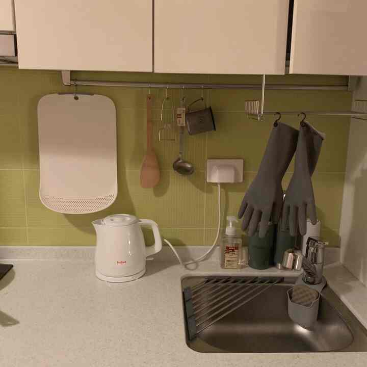Compact kitchen sink space in white and silver tones, featuring shelves and a foldable dish dryer arranged for efficient use