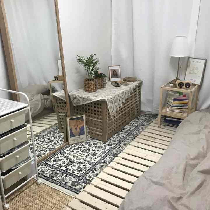 ナチュラルな木目調とシンプルな配置の寝室、壁に立てかけられた大きな全身鏡とサイドテーブル、ホワイトの遮光カーテンが配置された雰囲気のあるインテリア