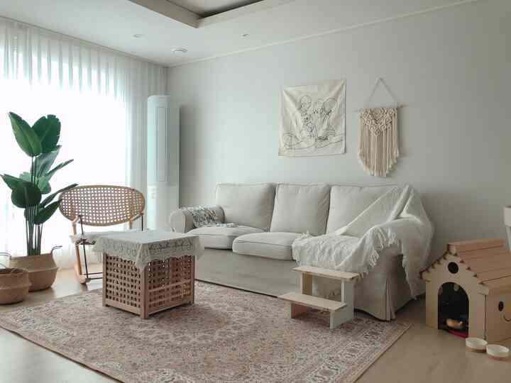 Bright natural-toned living room featuring beige sofa and rug centered with drawing poster and macramé wall hanging adorning the wall, creating cozy atmosphere
