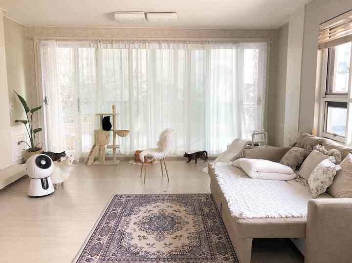 明るいホワイトトーンのリビング、ベージュのソファと柄付きラグが配置されたヴィンテージスタイルの空間