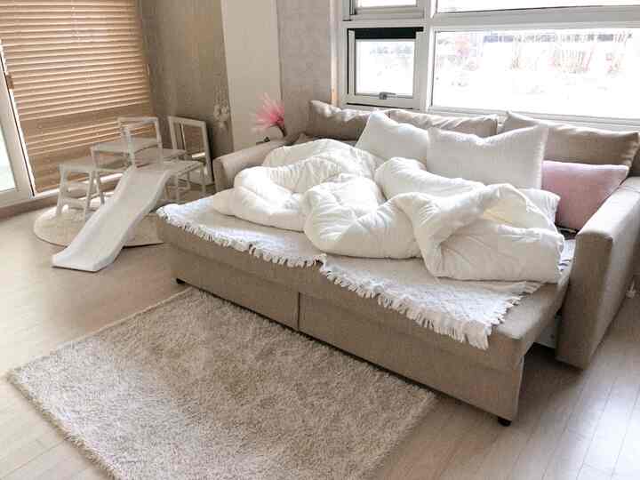 ナチュラルなベージュと木目調のリビング、ベージュのフリヘーテンソファとシャギーラグ、子供の遊具が配置された雰囲気のあるインテリア