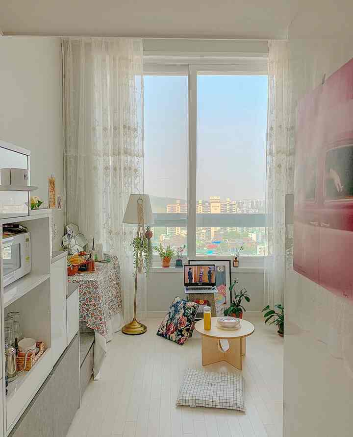 明るいホワイトとベージュのワンルーム、木製の小さなテーブル、レースカーテンと植物が配置された落ち着いたおうちカフェの雰囲気のあるインテリア