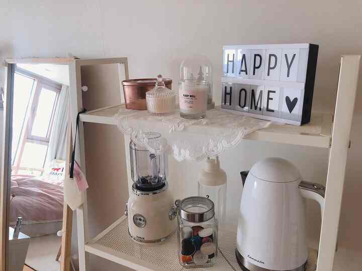 White-toned studio apartment kitchen shelf featuring a blender, electric kettle, and candles arranged in a cozy setting
