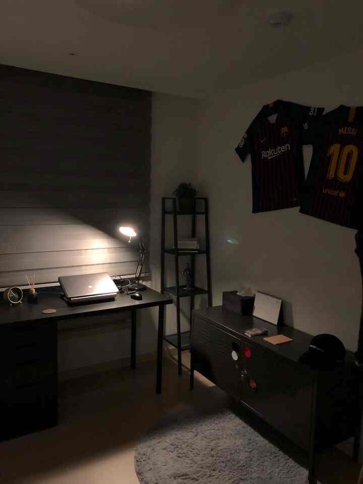 黒と灰色のモノトーンでまとめられた狭いホームオフィス書斎、コンピューターデスクと金属キャビネット、ラグが配置されたモダンなインテリア