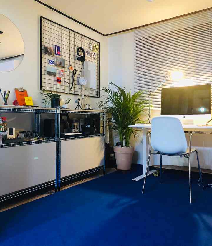 A clean home office with white and deep blue tones, featuring a desk with computer and shelving in a workspace setting