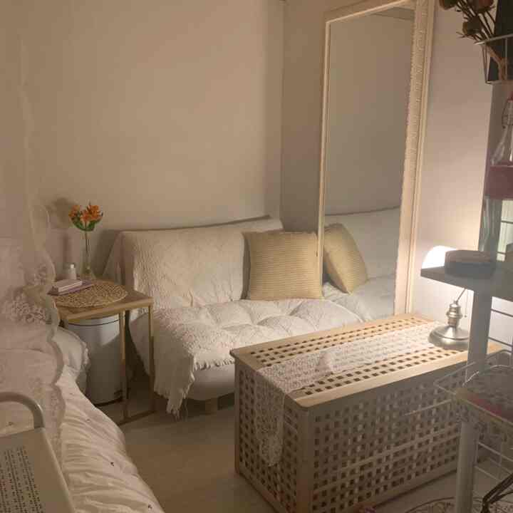 Cozy small studio apartment in white and beige tones featuring lace-covered sofa, large mirror, and natural wood table