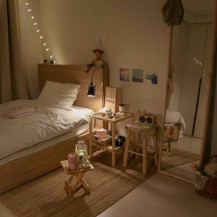 ナチュラルな木目調と白のワンルーム寝室、サイドテーブルとスツールが配置された居心地の良い空間