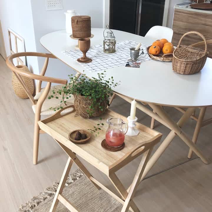 ナチュラルな木目調とホワイトの調和が美しいキッチンダイニングテーブルと折りたたみテーブル、トレイが配置された雰囲気のあるおうちカフェ空間