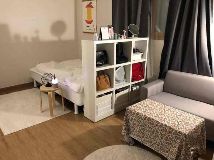 A cozy studio apartment with white and brown tones, featuring a bedroom and living room separated by a dresser