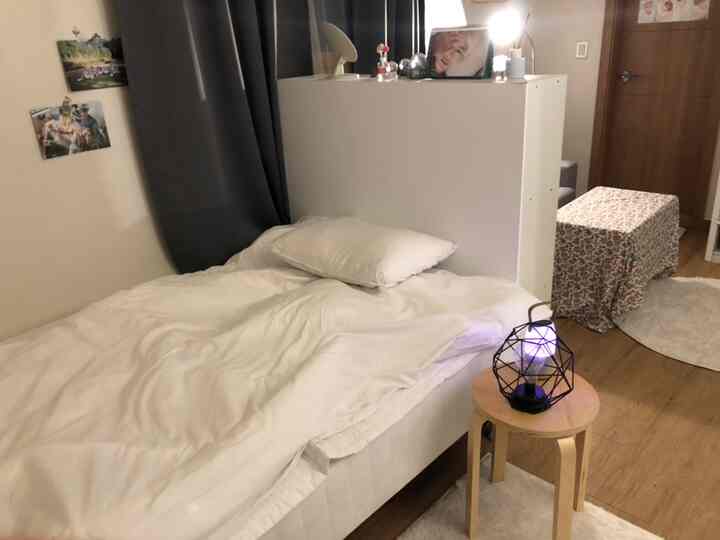 White bedding and blackout curtains in a studio bedroom space, with a bookshelf used as room divider creating a neat and practical atmosphere.