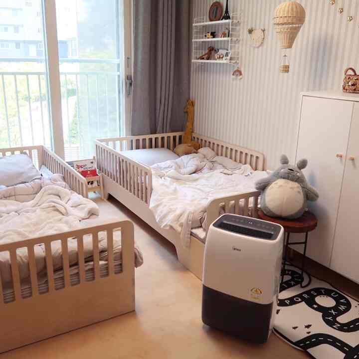 ナチュラルな色調と木製家具の子供部屋、2つの子供用ベッドとベビー寝具が見える温かみのある整った空間