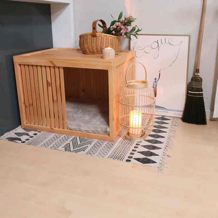 Natural-toned living room corner featuring a wooden dog house, bamboo candle holder, and leather strap basket with flowers in a simple setting