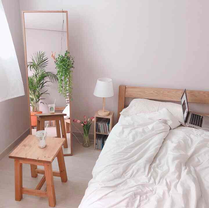 Bright bedroom with white and natural wood tones featuring a bed, full-length mirror, and plants creating a minimalist atmosphere