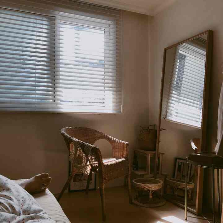 暖かいナチュラルカラーの寝室、ラタンの椅子とバスケット、全身鏡が配置された雰囲気のあるインテリア