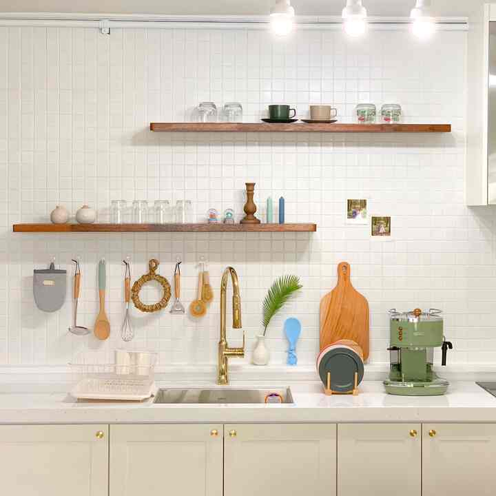 Bright and clean kitchen with white tiled wall and wooden shelves, featuring a gold faucet and vintage green coffee machine