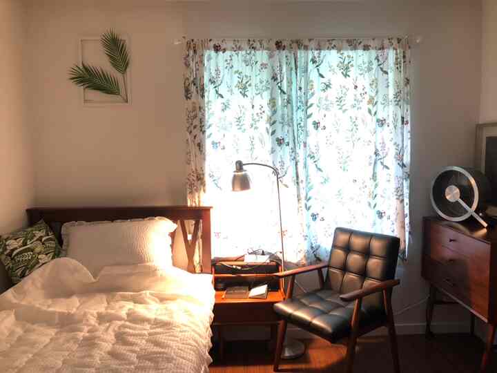 A white and wood tone bedroom featuring a bed, side table, and armchair with a retro vibe