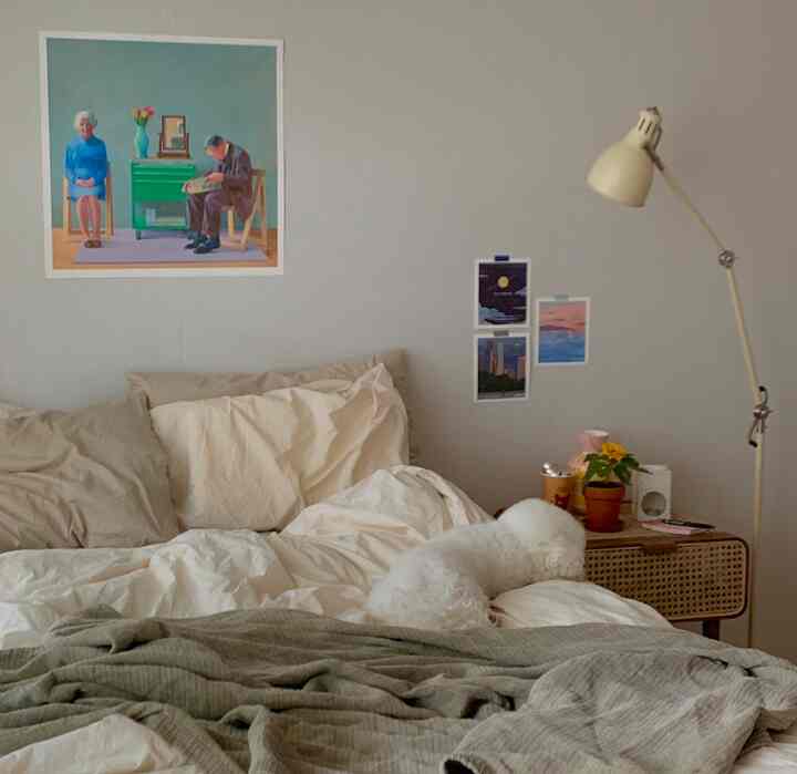 ベージュのナチュラルな寝室、ラタンのナイトテーブルとフロアランプ、小さな白い犬がいる温かみのあるインテリア