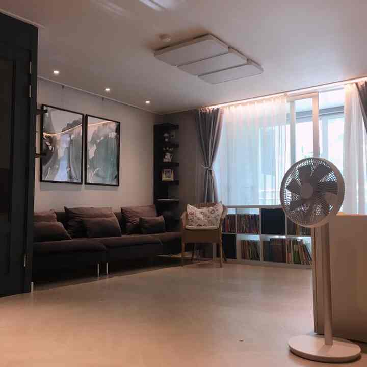 Modern living room in brown and black tones featuring dark sofa, armchair, long curtains, and a smart wireless fan in a tidy setting