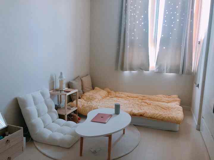White and beige toned small bedroom featuring a floor chair and low table with a cozy atmosphere