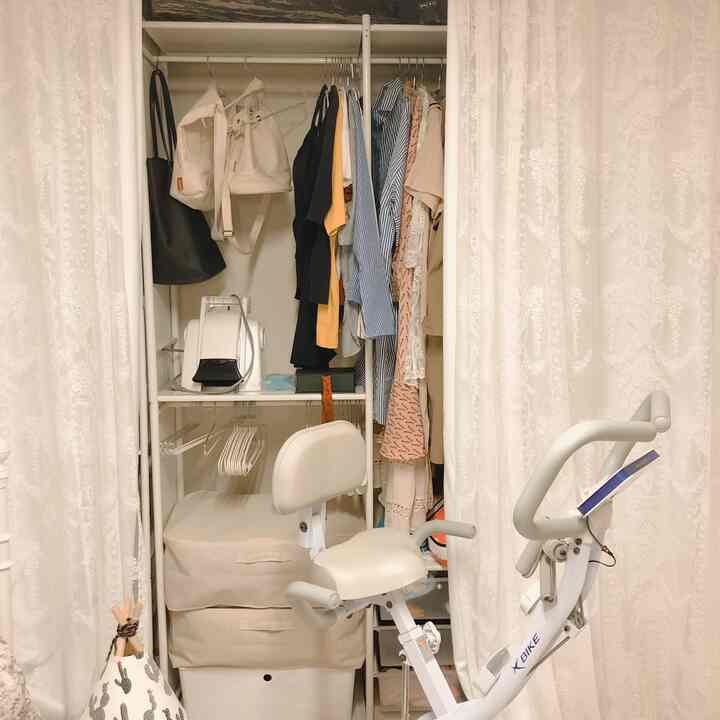 White and beige toned walk-in closet with lace curtains concealing Huseyn hangers and an exercise bike creating a cozy atmosphere