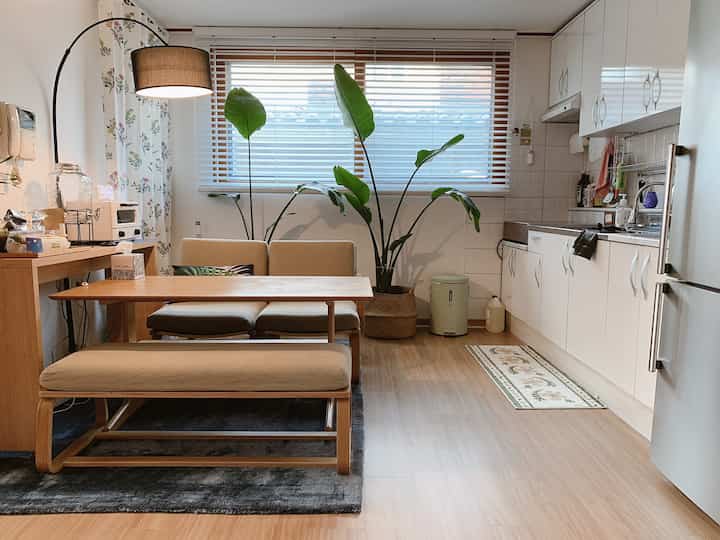 White and wood tone 20-pyeong villa living room and kitchen space with green plants harmoniously arranged