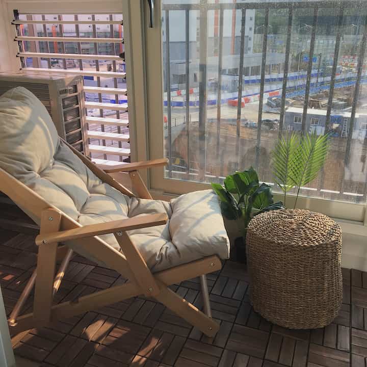 Balcony space featuring a beige cushioned wooden folding relax chair and natural material pouf with plants
