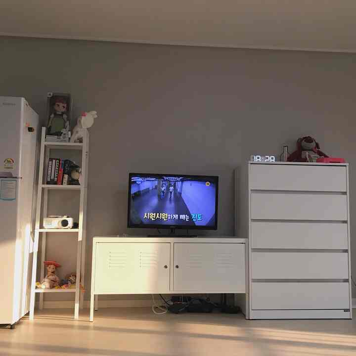 Bright studio apartment featuring white furniture and natural-toned flooring with neatly arranged TV and storage units