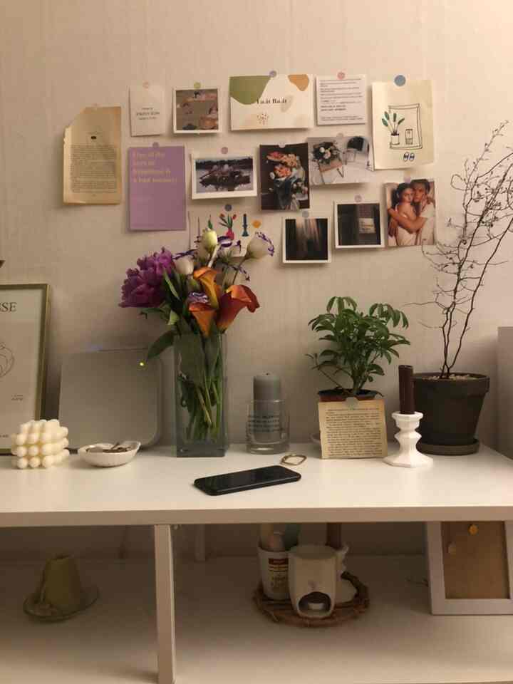 ベージュの壁と白いテーブル上に花瓶とキャンドル、植物が配置されたナチュラルでシンプルなインテリア空間