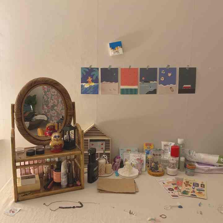 Natural color-toned studio apartment desk featuring rattan shelf, posters, candles, and various accessories creating a cozy atmosphere