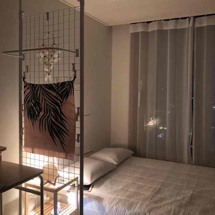 Soft white-toned bedroom featuring a neatly made bed and metal grid storage rack creating a cozy atmosphere