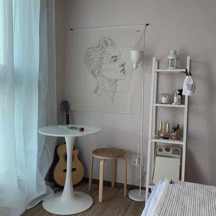 Natural-toned small room featuring white round table, beige rattan stool, fabric poster, and floor lamp creating cozy atmosphere