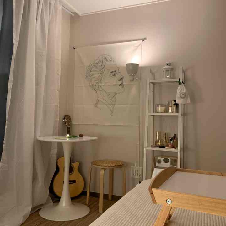 White and natural-toned bedroom featuring a small minimal stool, round table, and shelf creating a warm atmosphere