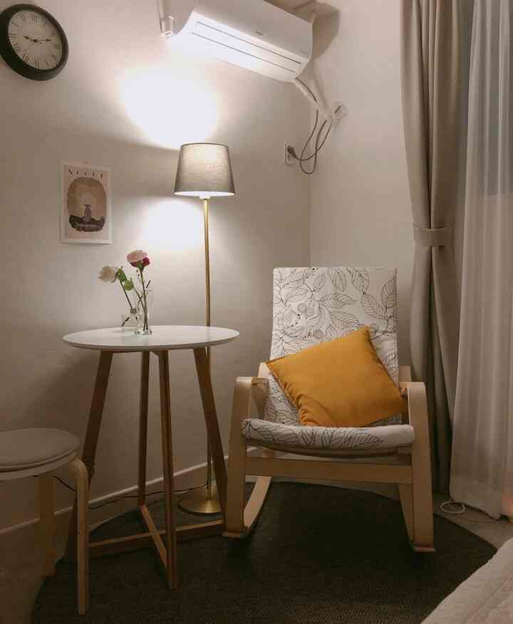 Warm brown and white toned single-person living room featuring wooden armchair, round table, and floor lamp for a cozy atmosphere