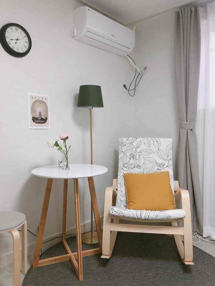 Beige-toned small living space featuring wood-tone armchair, round white table, and green floor lamp creating a cozy atmosphere