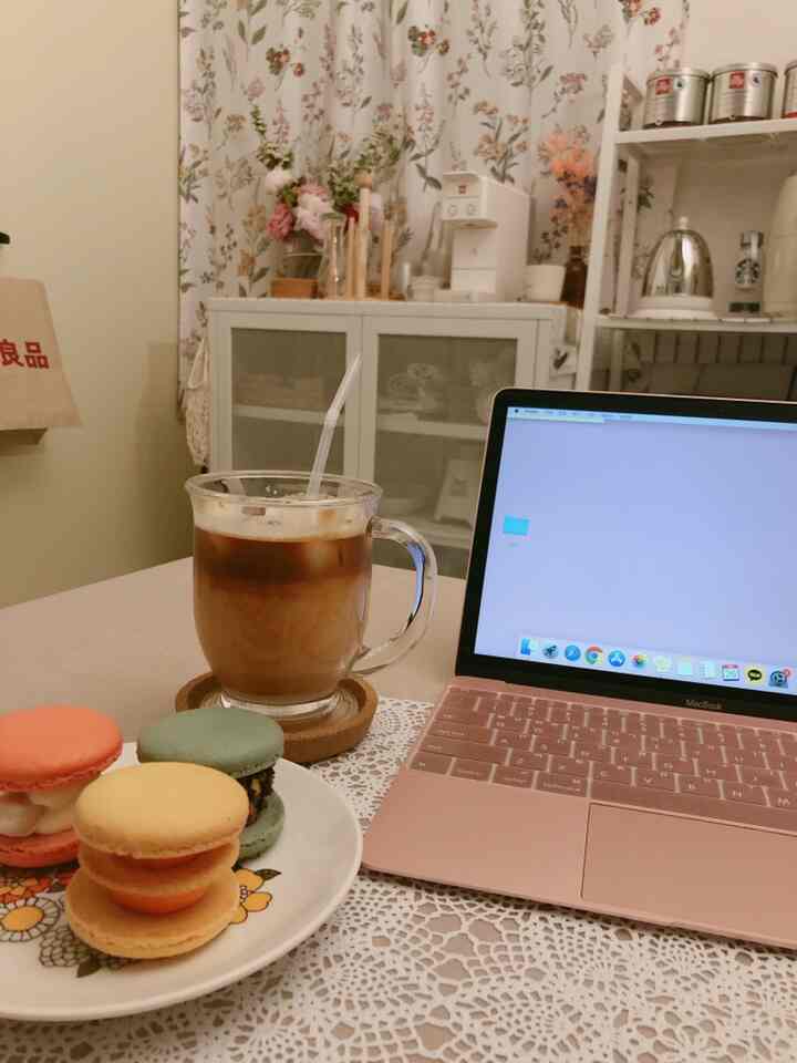 Natural toned compact room featuring floral curtains, storage cabinet, coffee, and macarons creating a cozy home cafe atmosphere