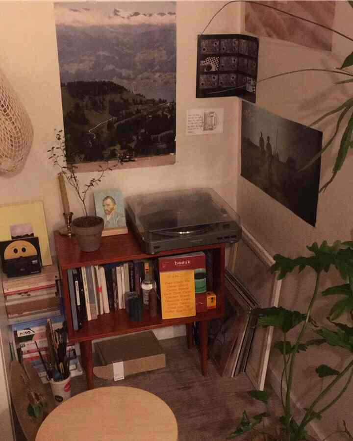 Cozy corner space featuring a wooden bookshelf with a turntable on top, surrounded by wall art, dominated by warm natural tones