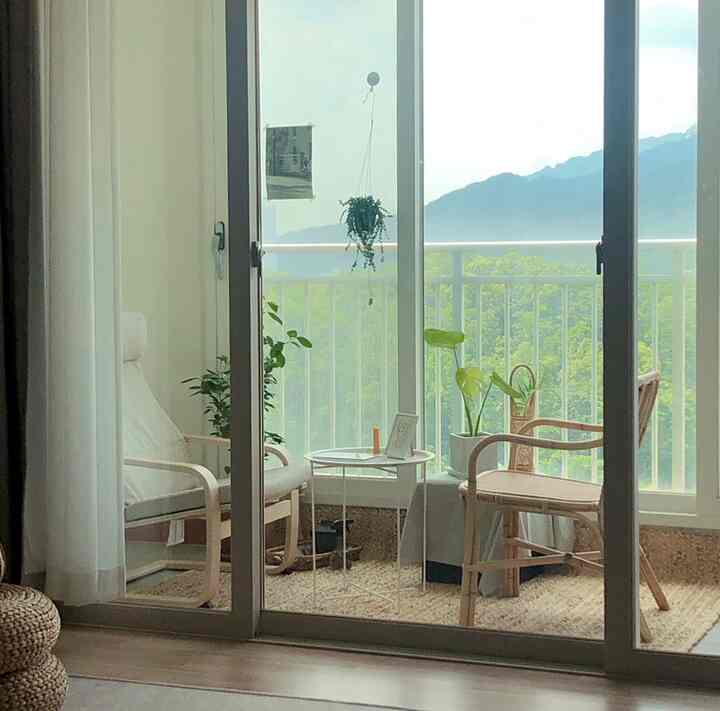 Natural-tone veranda space featuring white armchair, rattan chair, side table and plants in a cozy home cafe setting.