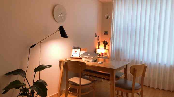 Cozy natural wood tone and white curtain two-person home office with floor lamp and wall clock accents